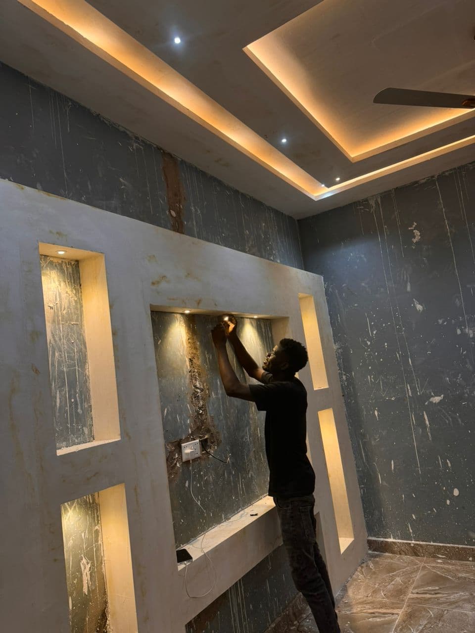 Electrician installing a recessed LED downlight into a gypsum feature wall with cove lighting