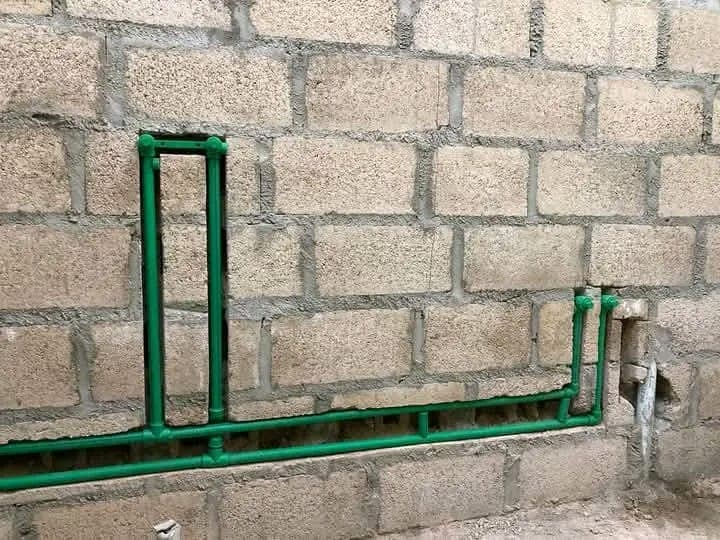 Green electrical conduit and plumbing pipes routed together along a block wall before plastering